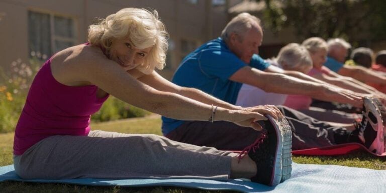 Group of Elderly Stretching Outdoors on Mats at Assisted Living Facility
